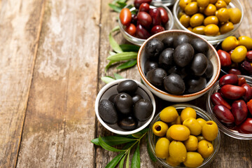 Green, black and red olives with leaves in bowls on a textured old wood background. Delicious and healthy food. Delicacy.Mediterranean Kitchen. Place for text. copyspace.