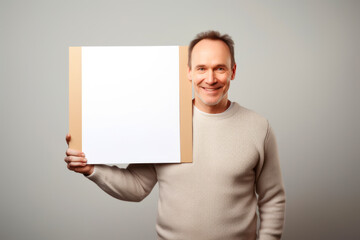 Portrait of a smiling man holding a blank sheet of paper on grey background