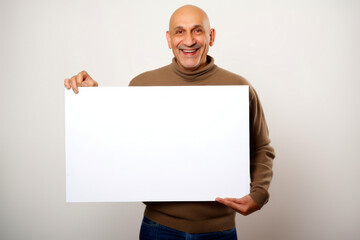 Portrait of a bald man in a beige sweater holding a white sheet of paper