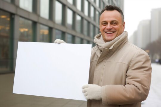 Portrait of a smiling man holding a blank sheet of paper outdoors