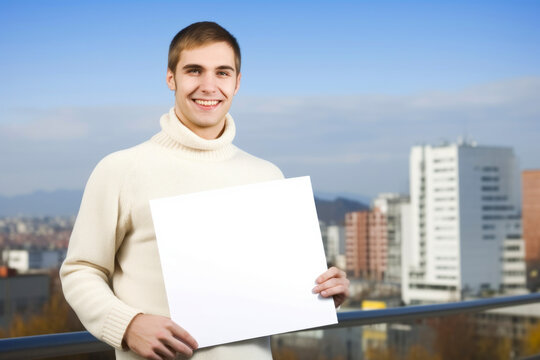Portrait of a happy young man holding blank sheet of paper outdoors