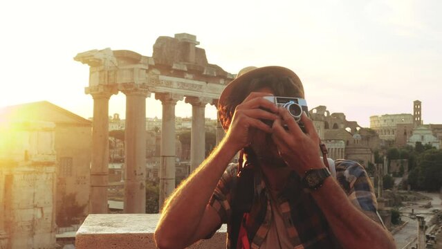 Young man tourist backpacker taking pictures with vintage camera at Roman Forum at sunrise. Historical imperial Foro Romano in Rome, Italy from panoramic point of view.