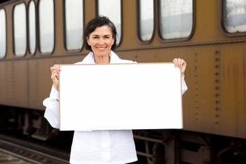 Group portrait photography of a pleased woman in her 50s holding an empty white blank sign poster wearing a chic cardigan against a vintage train or railway background