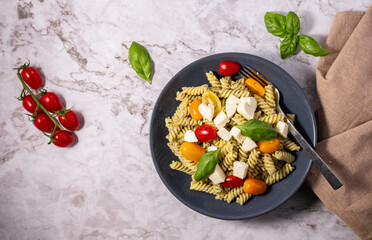 Fresh pesto pasta salad with different colours of cherry tomatoes and mozzarella with a light background.