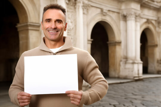 Handsome man holding a blank sheet of paper in a city street