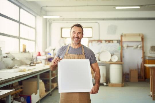 Portrait of a smiling male worker holding a whiteboard in a factory