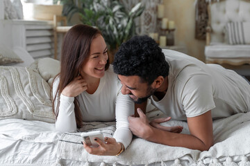 Multiethnic American couple using smartphone lying on bed together