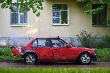 An old rusty red wrecked car abandoned against the wall of a residential building, Gromova Street, St. Petersburg, Russia, May 2023