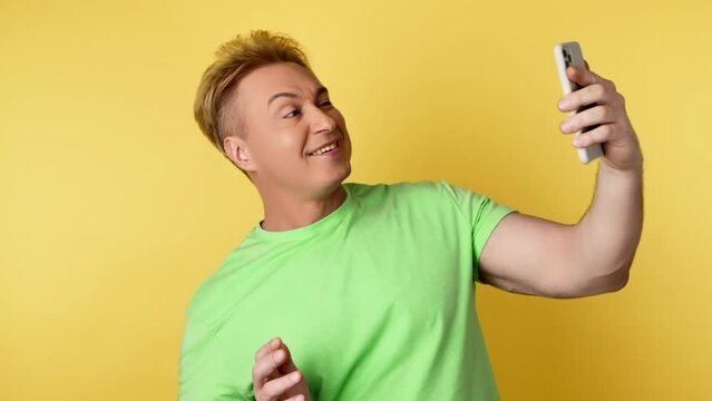 Selfie, pose and man with phone, peace sign for social media post. Positive guy with mobile smartphone posing smiling, taking profile picture, studio shot isolated on yellow background