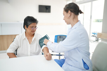 Female doctor doctor measuring senior female's blood pressure at medical clinic.