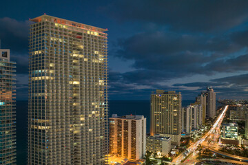 Fototapeta na wymiar Night urban landscape of downtown district in Sunny Isles Beach city in Florida, USA. Skyline with brightly illuminated streets and high skyscraper buildings in modern american megapolis