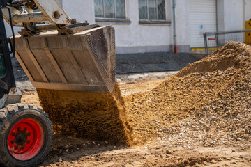 Construction dumper dumping gravel in construction site from the side in a sunny day. Hard business