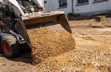 Fototapeta na wymiar Skid steer loader loading ground and gravel with metal bucket in construction yard next to a building close up