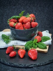 Graue Schale mit frischen Erdbeeren und grüner Minze serviert auf einem Holzbrett mit dunklem Hintergrund