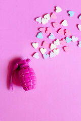 Pink toy hand grenade bomb with multicoloured small hearts on a pink background. The concept of peace and life without war. Make Love Not War