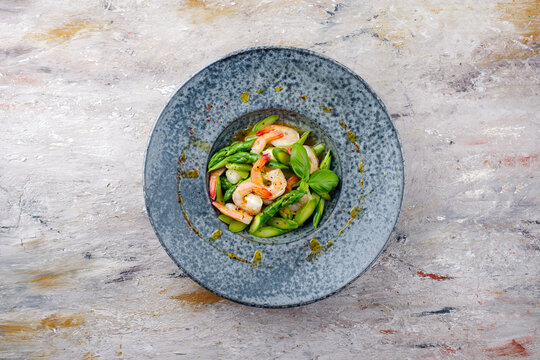 Gr&uuml;ner Spargel Salat ged&auml;mpft als Spitzen und Scheiben mit Garnelen und Passionsfrucht Vinaigrette serviert als Draufsicht auf einem Nordic Design Teller mit Textfreiraum