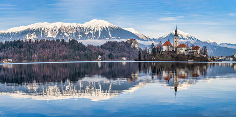 Panorama shot of lake Bled island church, bled castle and snow peak mountains during a winter afternoon, Bled, Slovenia