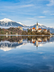 Lake Bled island church, bled castle and snow peak mountains reflection on water during a winter...