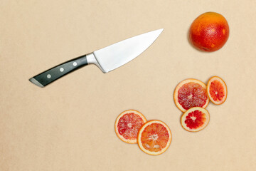 Ripe blood sicilian orange running away from knife cutting it.beige background.Concept of citrus...