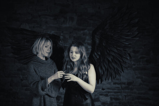Cigarette temptation. A woman passes a cigarette to an angel with black wings and red hair. Black and white image.
