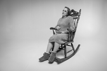 Fototapeta na wymiar black and white portrait of a pregnant woman resting on a wooden rocking chair on a light background, expectant mother, full length photo, place for text