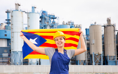 Cheerful female worker in hardhat with catalan flag standing in front of factory