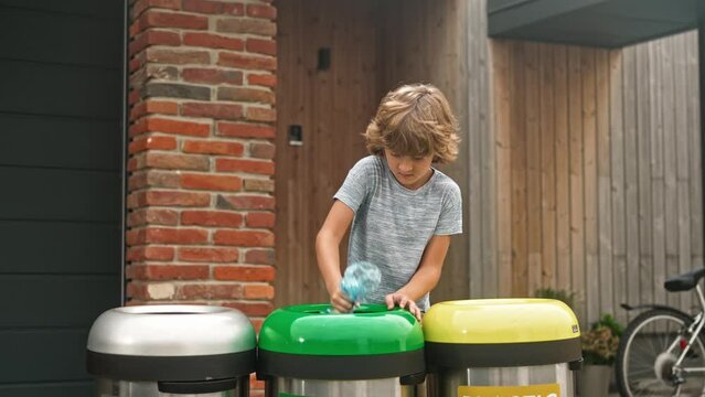 Portrait of pre-adolescent boy throwing plastic and glass bottles in dustbin for recycling near parents home. Environmental care. Emty bottles. Ecological garbage recycle. Modern domestic lifestyle.
