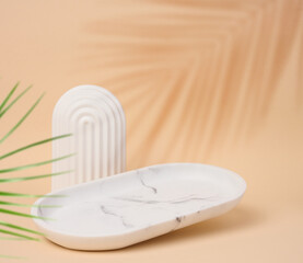 Empty oval white marble stand on a beige background and a shadow from palm leaves, a place to display cosmetics and products