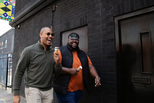 Two smiling men in front of black wall enjoying ice cream 
