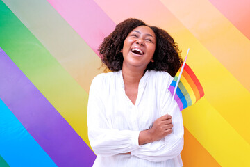 African woman portrait American is standing smiling and laughing while holding a rainbow flag that symbolizes her lgbt, equality, freedom, lgbt concept.
