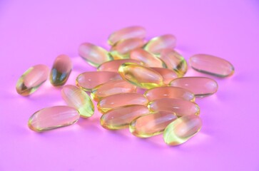 Obraz na płótnie Canvas Transparent yellow omega capsules (pills) on a pink purple neon background, closeup