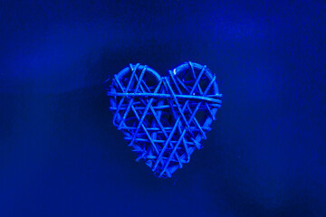Wooden wicker heart. Rattan work in the shape of a heart. Love concept. Background with selective focus. On colored foil
