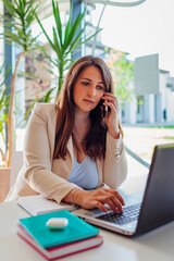 Female office worker talking on smartphone using laptop. Young businesswoman working online through modern technologies