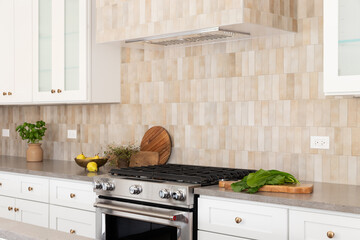 A kitchen oven and hood detail with brown rectangle tiles, stainless steel oven, white cabinets,...