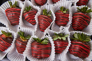 Wall of multiple dark chocolate-covered strawberries with green tuffs and red frosting drizzle