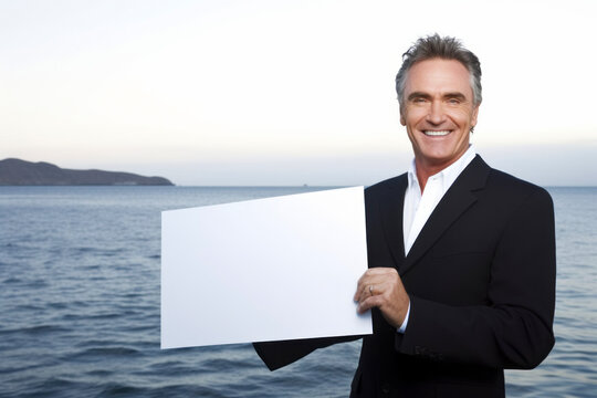 Mature businessman holding a blank placard in front of the sea