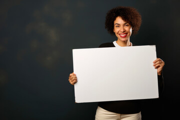 Young african american woman holding a blank board on dark background