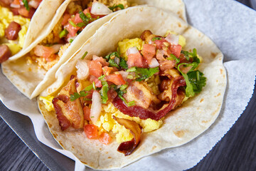 Mexican breakfast three tacos sausage egg bacon tomato chives flour tortillas food on white paper