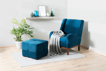 a blue chair sits near a plant on a rug near referred a shelf with a