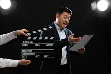 Emotional asian actor performing role while second assistant camera holding clapperboard on stage,...