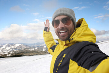 Fototapeta na wymiar Smiling man in sunglasses taking selfie in mountains