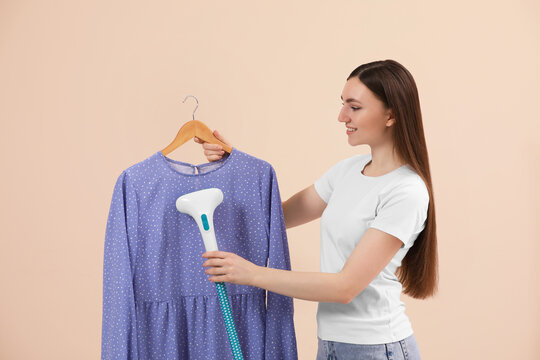 Woman steaming blouse on hanger against beige background
