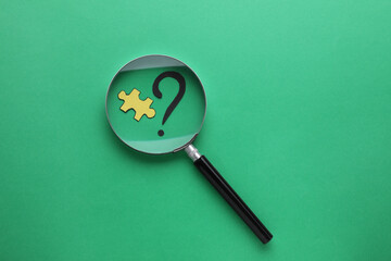 Magnifying glass over paper puzzle and question mark on green background, top view