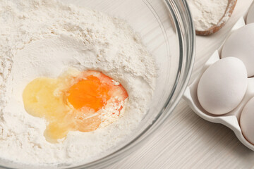 Bowl with flour and egg on white wooden table, closeup