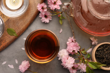 Obraz na płótnie Canvas Traditional ceremony. Cup of brewed tea, teapot and sakura flowers on grey table, flat lay