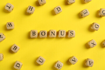Word Bonus made of wooden cubes with letters on yellow background, flat lay