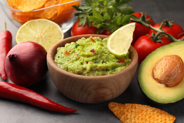 Bowl of delicious guacamole, nachos chips and ingredients on grey table, closeup