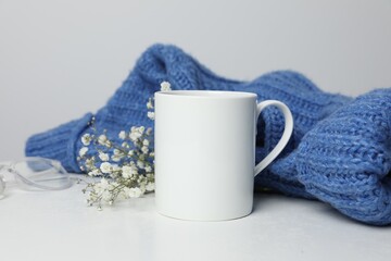 Ceramic mug, blue knitted sweater, glasses and beautiful dry flowers on white table