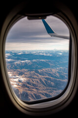 View of the snow covered Andes Mountains through the window of an airplane at sunrise