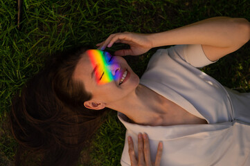 Top view of caucasian woman with rainbow ray on her face lies on green grass. 